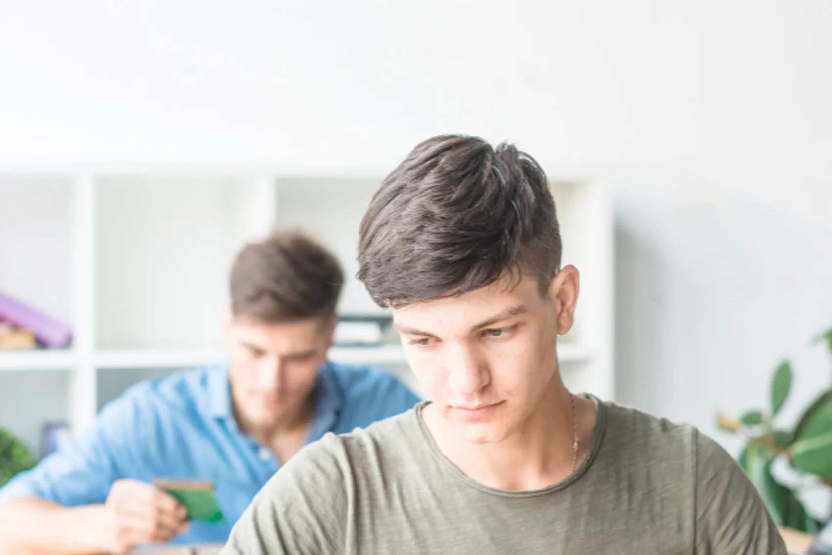 Um jovem está a trabalhar simultaneamente em um tablet (disposito digital) e um circuito elétrico. Há um outro jovem e uma fileira atrás também a trabalhar em em um circuito elétrico
